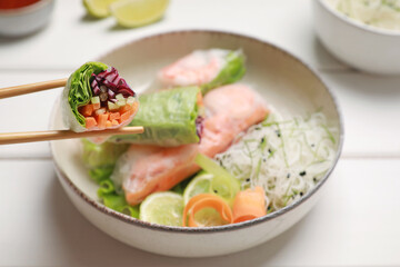 Delicious spring rolls wrapped in rice paper on white wooden table, closeup