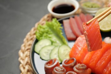 Taking tasty salmon slice with chopsticks at table, closeup. Delicious sashimi dish