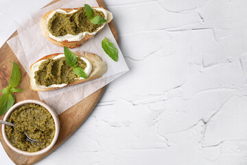Tasty bruschettas with cream cheese, pesto sauce and fresh basil on white textured table, top view. Space for text