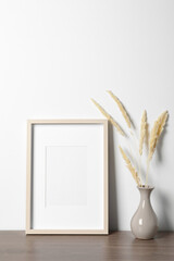 Empty photo frame and vase with dry decorative spikes on wooden table. Mockup for design