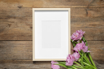 Empty photo frame and beautiful flowers on wooden table, flat lay. Space for design