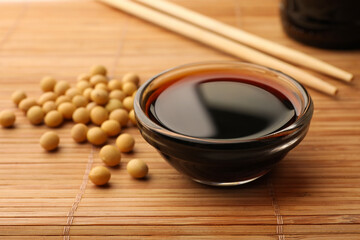 Soy sauce in bowl and soybeans on bamboo mat, closeup