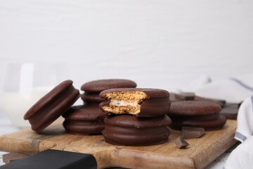 Tasty choco pies and pieces of chocolate on wooden board, closeup. Space for text