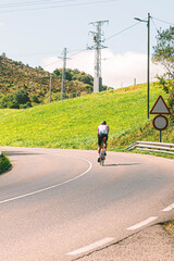 Vertical photo of a sporty man with a cycling jersey doing a tough road route in Asturias in a sunny summer day to feel healthy and fit