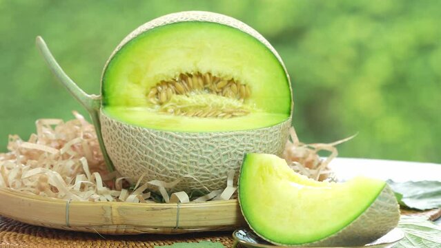 Crown Musk Melon on blurred greenery background, Cantaloupe Crown Melon fruit in Bamboo mat on wooden table in garden.