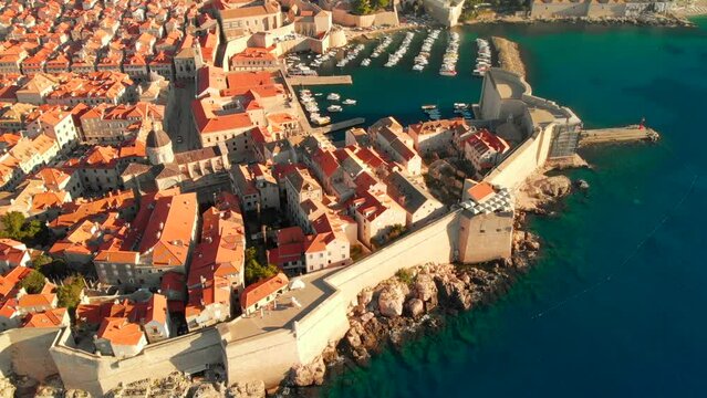 An aerial view of a Dubrovnik Old Town. The walls and historic old town can be seen in this drone clip. A swimmer is outside the walls