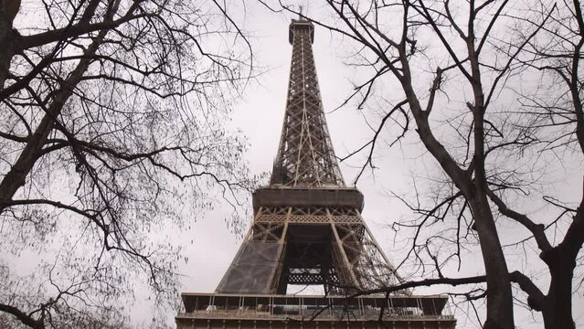 Low Angle, Tilt Up View of Eiffel Tower Through Trees in City of Paris on Cloudy Day
