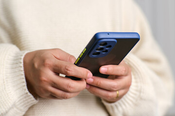 Closeup of female hand holding smartphone checking social media, playing games, online shopping relaxing on sofa. Lifestyle, free time and relaxation.