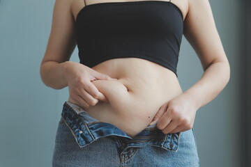 Close up of a belly with scar from c-section and abdominal fat. Women's health. A woman dressed up in sportswear demonstrating her imperfect body after a childbirth with nursery on the background.
