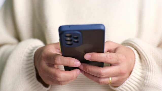 Closeup of female hand holding smartphone checking social media, playing games, online shopping relaxing on sofa. Lifestyle, free time and relaxation.