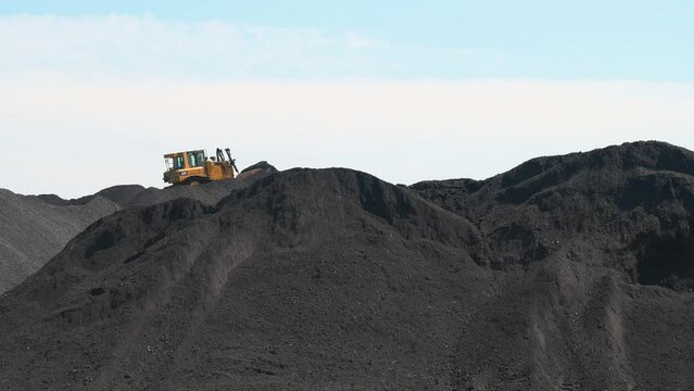 Wide shot of a digger working on mountains of coal being prepared for a power plant.