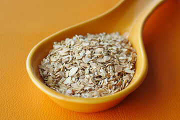 roasted oats flakes in a spoon on orange color background 
