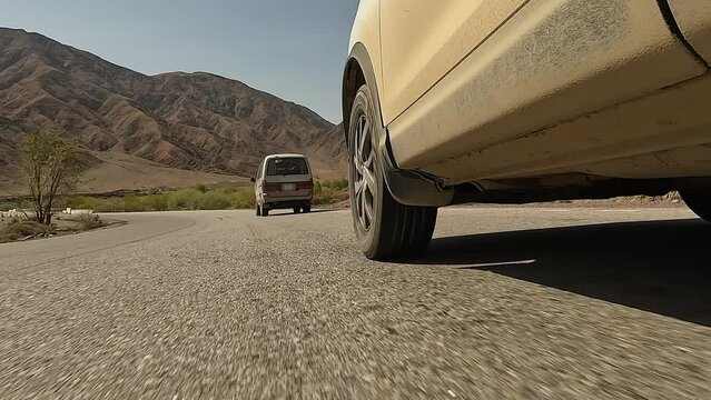 Bottom view of the left front wheel of an SUV and a minivan moving in front. Traveling by car in Kyrgyzstan. An exciting road adventure.