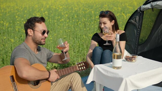 Happy young couple clinking wine glasses during camping in rural countryside by yellow flowring field