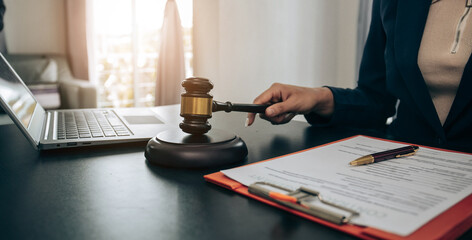 Beautiful young woman lawyer sitting in front of laptop in room with documents and smartphone with empty hammer and scale next to it justice and legal concept