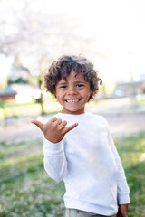 Cute African American little boy making a hang loose hand sign showing that he is happy and feeling good. Selective focus on his hand. Outdoors in good weather having fun