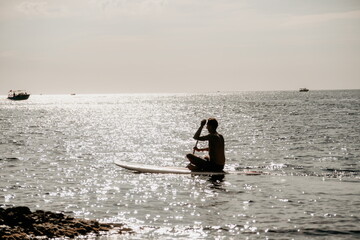 Naklejka premium Side view foto of a man swiming and relaxing on the sup board. Sportive man in the sea on the Stand Up Paddle Board SUP. The concept of an active and healthy life in harmony with nature.