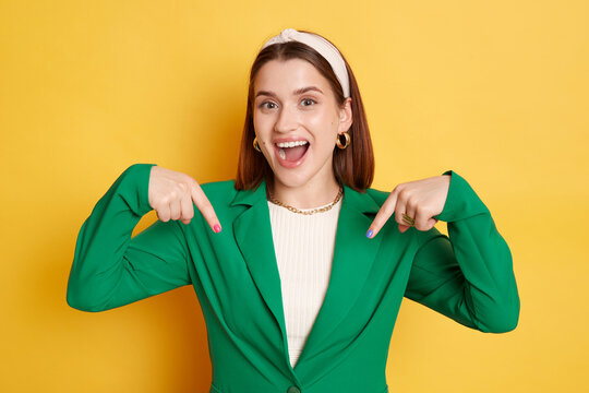 Overjoyed attractive woman wearing green jacket posing isolated over yellow background pointing up asking to subscribe her blog looking at camera with happy face. - Powered by Adobe