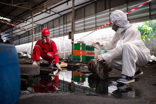 Worker or scientist industry wearing protective safety uniform, white glove and gas mask under cleaning up and lapping spilled oil in factory area to check in laboratory is industry safety concept.