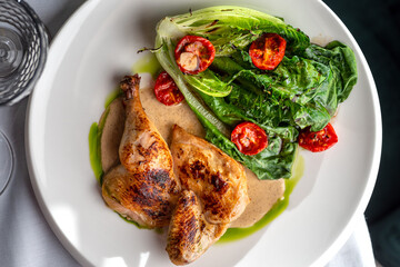 Half of a roasted chicken, on plate with herbs and tomatoes.
