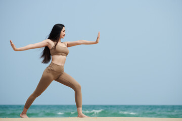 Fototapeta na wymiar Young woman practicing yoga on sandy beach in the morning