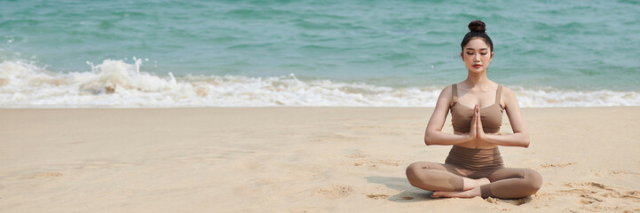 Fototapeta na wymiar Header with young woman meditating in lotus position on sandy beach