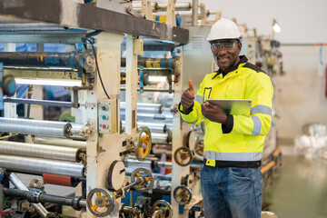 african engineer Wear uniforms and helmets. Stand with a confident thumbs up and smile. in hand a tablet And around there are machines working on steel and plastic production. in the industrial plant