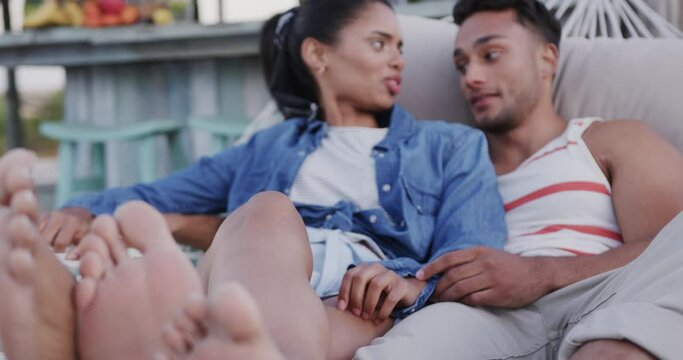 Happy diverse couple relaxing in hammock together and talking at beach bar, in slow motion
