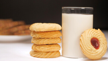 A beautiful shot of cookie topped with jam dipped in a glass of warm milk. Closeup shot of few biscuits with a glass full of fresh milk against a black background - common breakfast