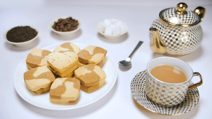 Elegant table decoration with designer tea-set  a plate of cookies  and sugar cubes. Closeup shot of a female's hand placing a heart-shaped cookie - arranging the breakfast table