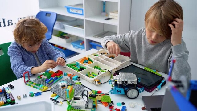 Robotics programming class. Children construct and code Robot. STEM education using constructor blocks and laptop tablet, remote control joystick. Technology educational development for school kids. 
