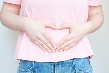 Female hands in the shape of heart on the stomach, concept of female health.