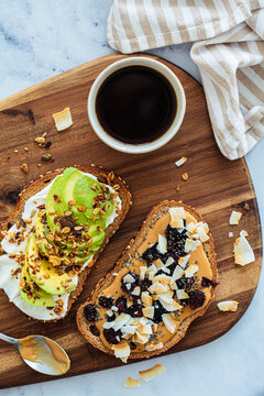 Vegan breakfast toasts with avocado and peanut butter on wooden board.