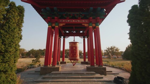 Red prayer drum kurde with golden buddhist symbols in a pagoda surrounded by trees