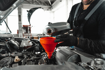 Close up of car service worker pouring new oil into car engine