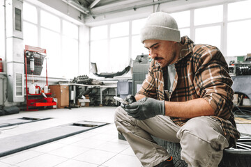 Car service worker sitting on a wheel and resting, using mobile phone