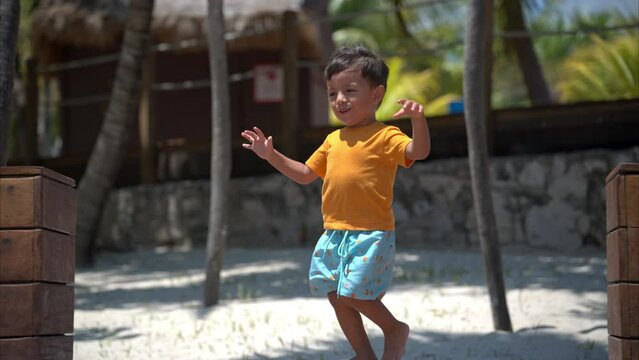 Happy latin hispanic toddler wearing shorts running and smiling barefoot at a beach in Cancun Mexico