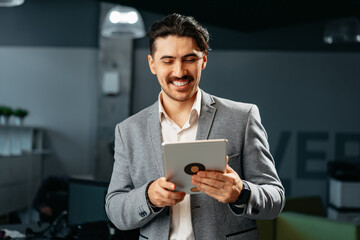 Young successful businessman working on digital tablet while standing in office