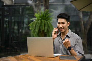 Cheerful and excited Asian businessman rejoicing while talking on the phone