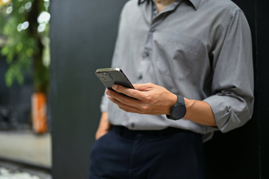 Cropped image of a businessman using his smartphone while standing outside of the building.