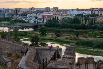 Obraz premium Dos turistas admirando el río Guadiana desde la Alcazaba árabe de Badajoz durante la puesta de sol.