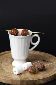 Beautiful white porcelain cup of hot Chocolate drink with marshmallows and chocolates skewers over wooden table on black background. Winter time. Holiday concept..