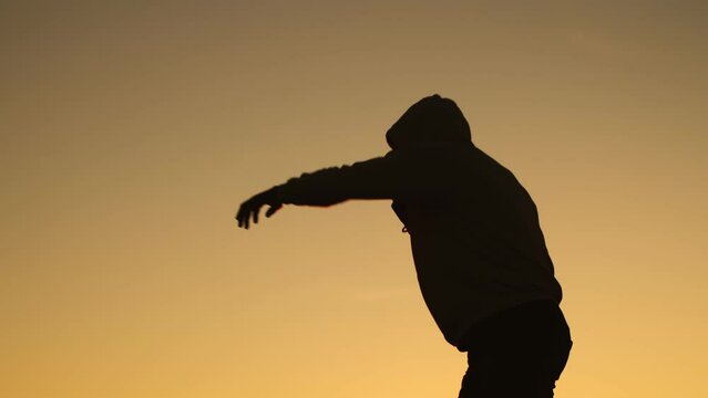 Black man athlete in hoodie struggles shadow fight background of sunset, side view. Male athlete training box, punches outdoor. Concept punch and workout