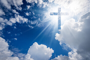Christian religious cross with sunbeams on a beautiful blue sky with white cumulus clouds and copy...