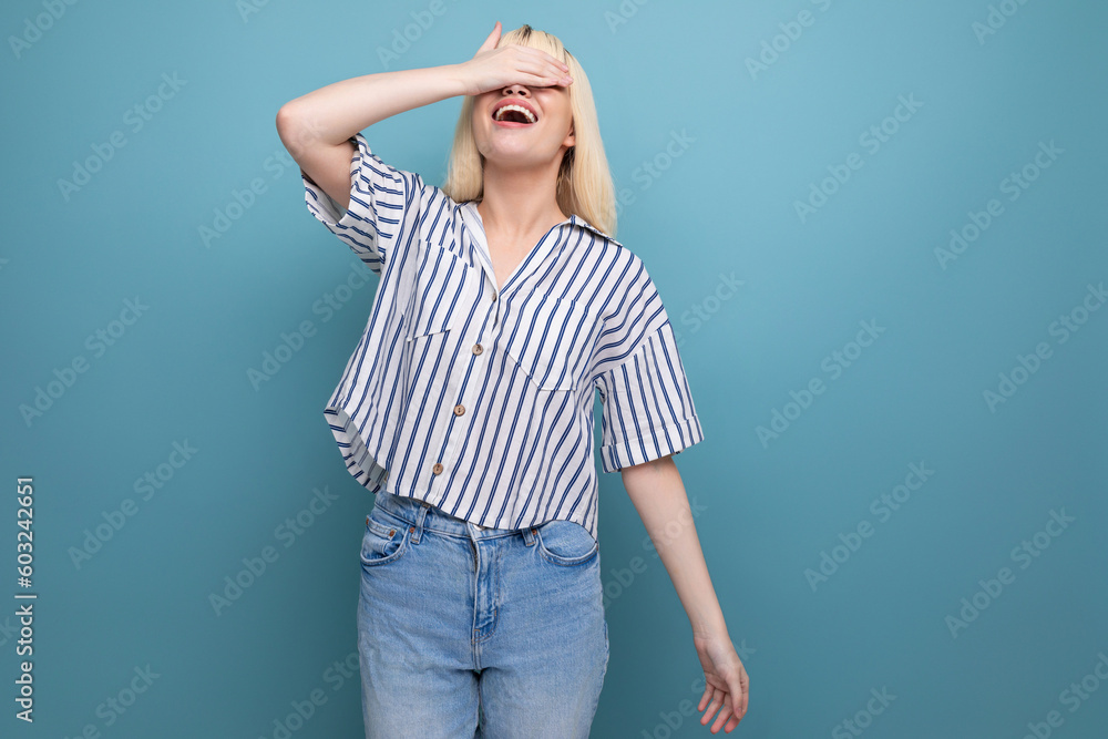 Wall mural cheerful cute blond 25 year old female person in a striped blouse and jeans on a blue background