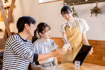 カフェ・レストラン・飲食店でスマホオーダー・タブレットオーダーをする男女と説明する店員
