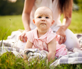 Little toddler baby learning to crawl on a picnic blanket in nature - Young tot girl on all fours smiling and looking on a blade of grass - Family outdoors concept with a little girl in a park