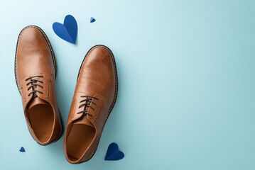 Father's Day surprise from little son. Top-down shot of dad's leather shoes, and hearts on pastel blue background with empty space