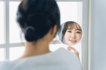 スキンケアをする鏡越しの笑顔のアジア人女性

