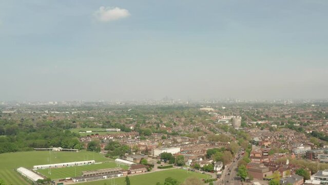 Descending aerial shot over Richmond recreational grounds and Twickenham road with London skyline in the background